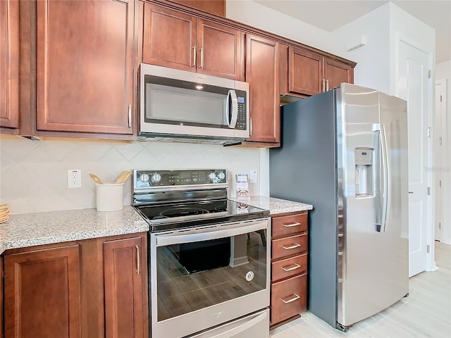 kitchen with light stone countertops, appliances with stainless steel finishes, tasteful backsplash, and light hardwood / wood-style floors