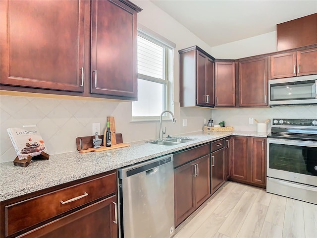 kitchen with light stone countertops, sink, decorative backsplash, appliances with stainless steel finishes, and light wood-type flooring