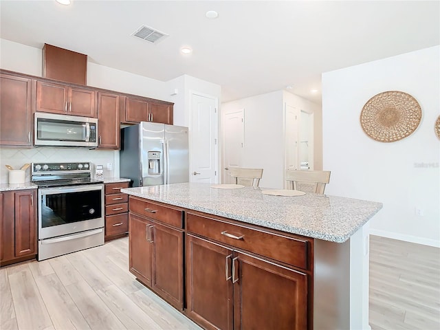 kitchen featuring decorative backsplash, appliances with stainless steel finishes, light wood-type flooring, light stone countertops, and a kitchen island