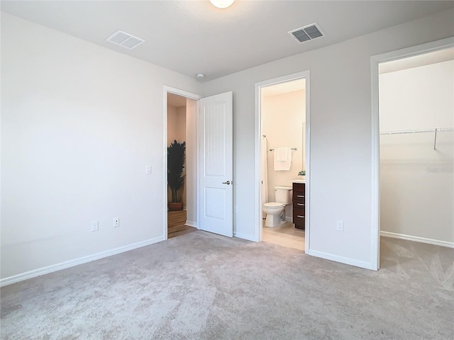 unfurnished bedroom featuring connected bathroom, a spacious closet, a closet, and light carpet