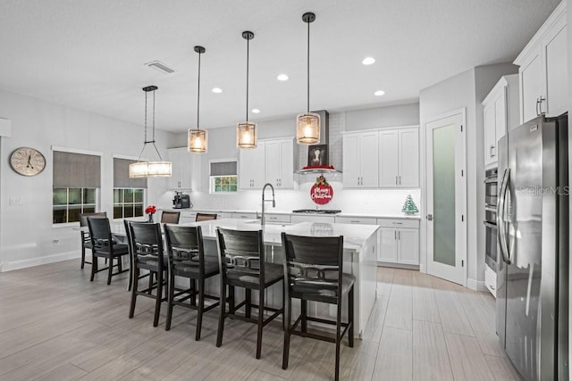 kitchen featuring white cabinetry, pendant lighting, stainless steel appliances, and a center island with sink