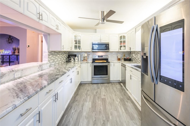 kitchen with white cabinets, appliances with stainless steel finishes, backsplash, and light hardwood / wood-style flooring