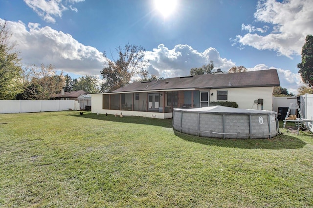 rear view of property featuring a sunroom, a fenced in pool, and a lawn