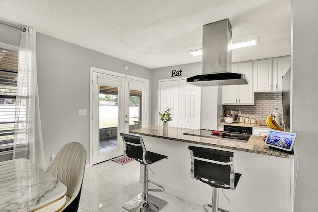 kitchen with french doors, a kitchen breakfast bar, island exhaust hood, dark stone counters, and white cabinets