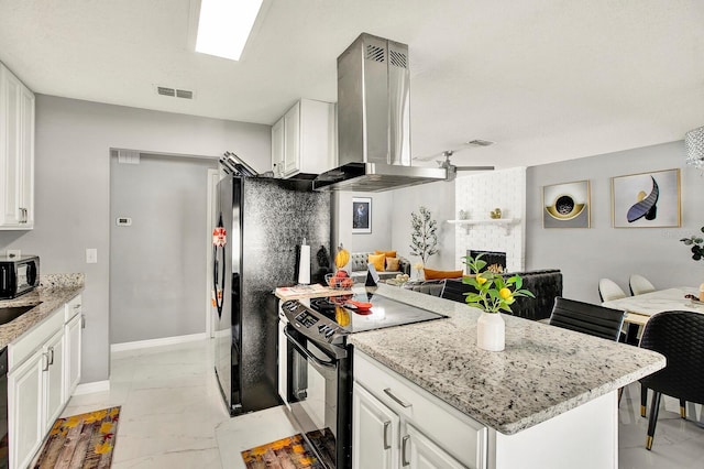 kitchen with light stone countertops, wall chimney range hood, a fireplace, white cabinets, and appliances with stainless steel finishes