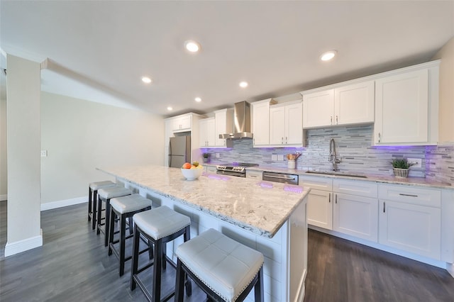 kitchen with dark hardwood / wood-style flooring, wall chimney exhaust hood, stainless steel appliances, white cabinetry, and a kitchen island