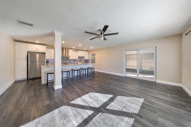 kitchen with white cabinetry, ceiling fan, dark wood-type flooring, stainless steel fridge, and a breakfast bar area