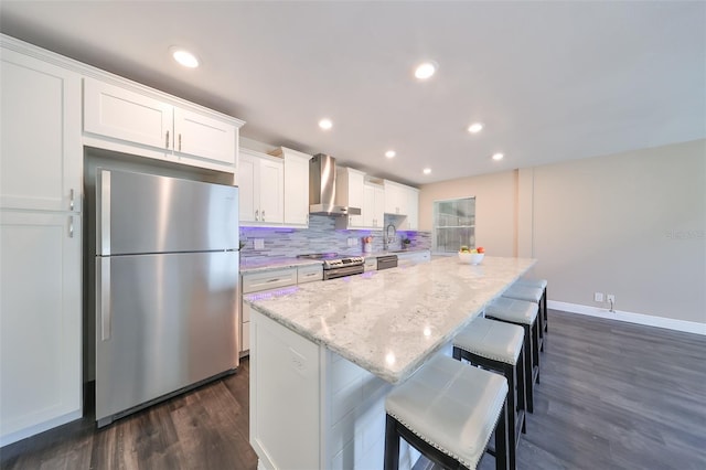 kitchen with wall chimney range hood, white cabinets, dark hardwood / wood-style floors, a kitchen island, and appliances with stainless steel finishes