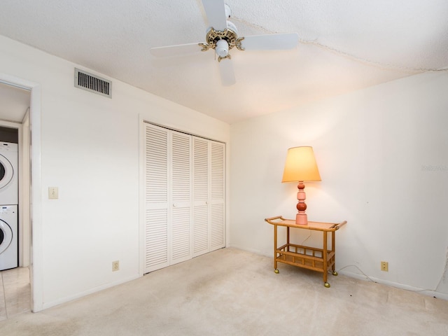 bedroom featuring stacked washer / drying machine, ceiling fan, light colored carpet, and a closet