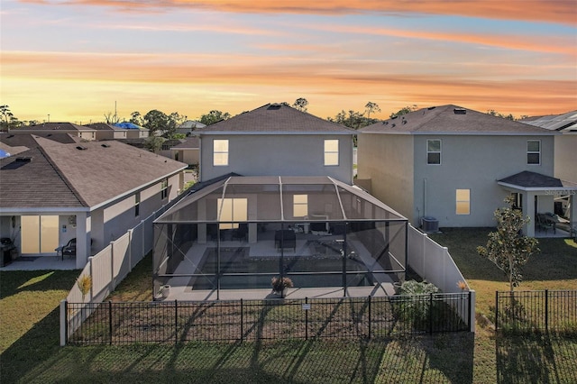 back house at dusk featuring a lawn, glass enclosure, a patio, and a swimming pool