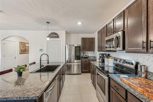 kitchen with sink, stainless steel appliances, an island with sink, dark stone counters, and dark brown cabinets