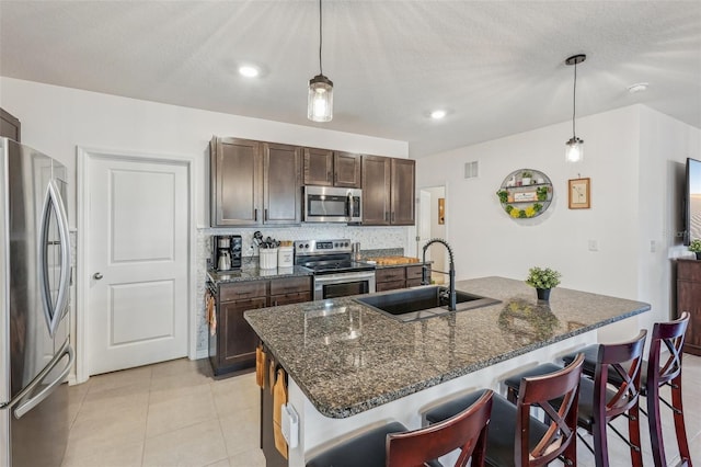 kitchen featuring decorative light fixtures, sink, stainless steel appliances, and an island with sink