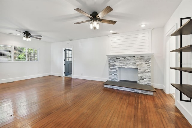 unfurnished living room with hardwood / wood-style flooring, a stone fireplace, and ceiling fan