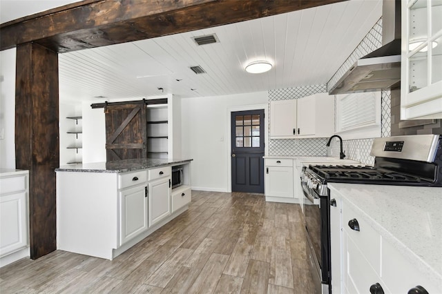 kitchen with a barn door, white cabinetry, appliances with stainless steel finishes, and dark stone counters