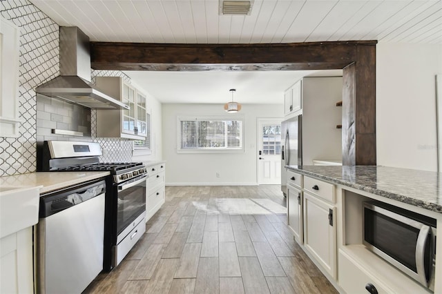 kitchen with hanging light fixtures, wall chimney exhaust hood, appliances with stainless steel finishes, light hardwood / wood-style floors, and white cabinetry