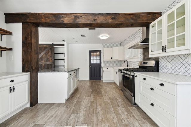 kitchen featuring light wood-type flooring, tasteful backsplash, wall chimney range hood, a barn door, and stainless steel gas stove