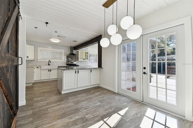 kitchen featuring wall chimney exhaust hood, stone countertops, light hardwood / wood-style flooring, white cabinets, and hanging light fixtures