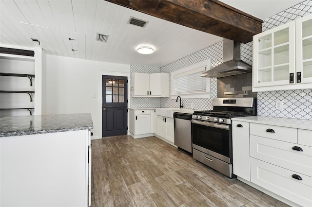 kitchen with decorative backsplash, light wood-type flooring, stainless steel appliances, wall chimney range hood, and white cabinets