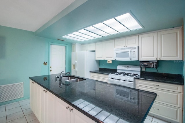 kitchen with white appliances, dark stone counters, white cabinets, sink, and light tile patterned flooring