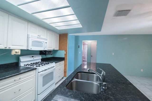 kitchen with white appliances, dark stone counters, sink, tile patterned flooring, and white cabinetry