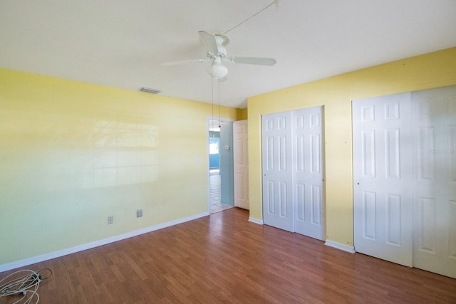 unfurnished bedroom with ceiling fan, two closets, and hardwood / wood-style flooring