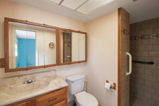 bathroom featuring a tile shower, vanity, and toilet