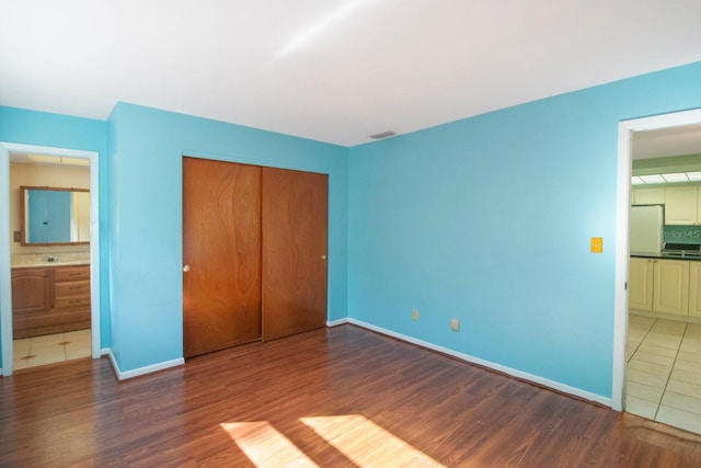 unfurnished bedroom featuring ensuite bath, a closet, white fridge, and dark wood-type flooring