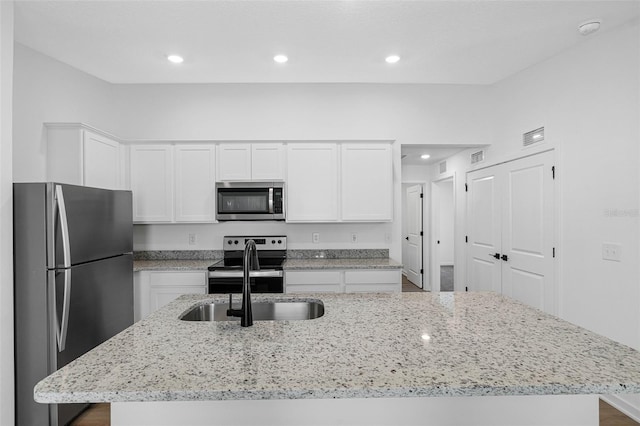 kitchen with light stone countertops, appliances with stainless steel finishes, sink, a center island with sink, and white cabinets