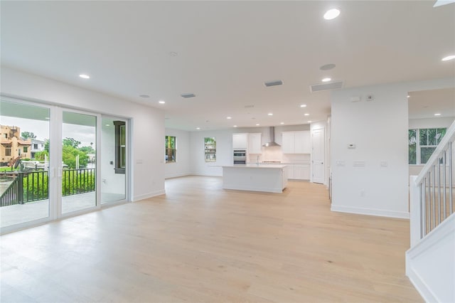 unfurnished living room featuring stairway, light wood-style flooring, baseboards, visible vents, and recessed lighting