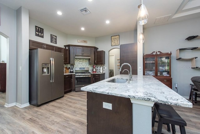 kitchen featuring light wood-type flooring, dark brown cabinetry, stainless steel appliances, sink, and hanging light fixtures