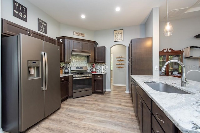 kitchen featuring light stone countertops, sink, stainless steel appliances, pendant lighting, and light wood-type flooring