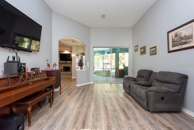 living room with light hardwood / wood-style floors, a stone fireplace, and a high ceiling