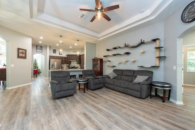 living room featuring a tray ceiling, ceiling fan, and light hardwood / wood-style flooring