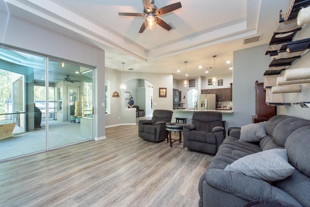 living room featuring a raised ceiling, ceiling fan, and light hardwood / wood-style flooring