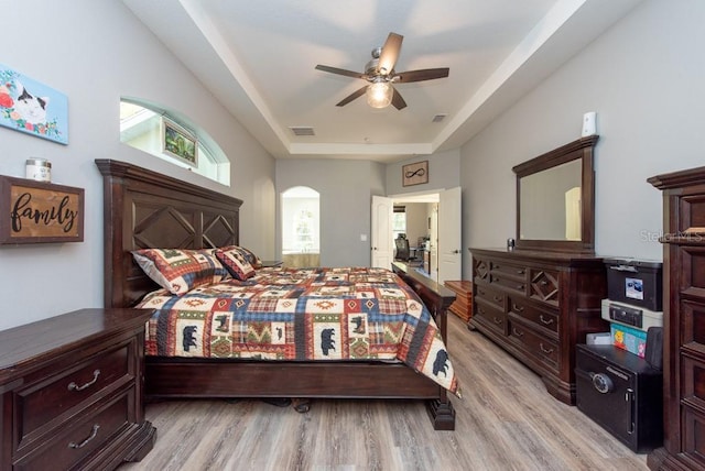 bedroom with a raised ceiling, ceiling fan, and light hardwood / wood-style floors