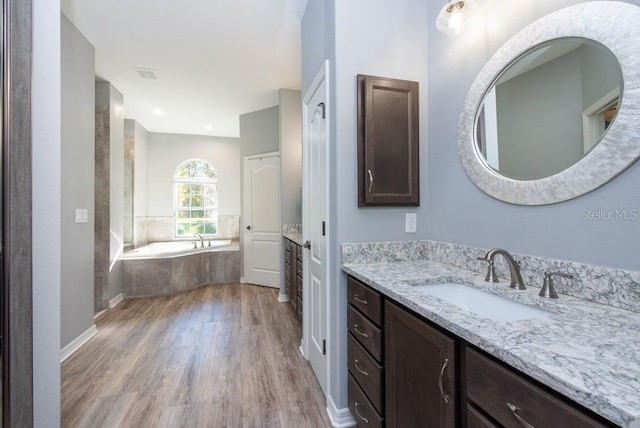 bathroom with tiled bath, hardwood / wood-style floors, and vanity