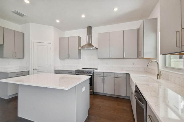 kitchen featuring gray cabinetry, sink, wall chimney exhaust hood, a kitchen island, and appliances with stainless steel finishes