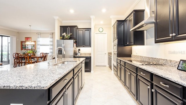 kitchen featuring stainless steel fridge, black electric cooktop, sink, wall chimney range hood, and an island with sink