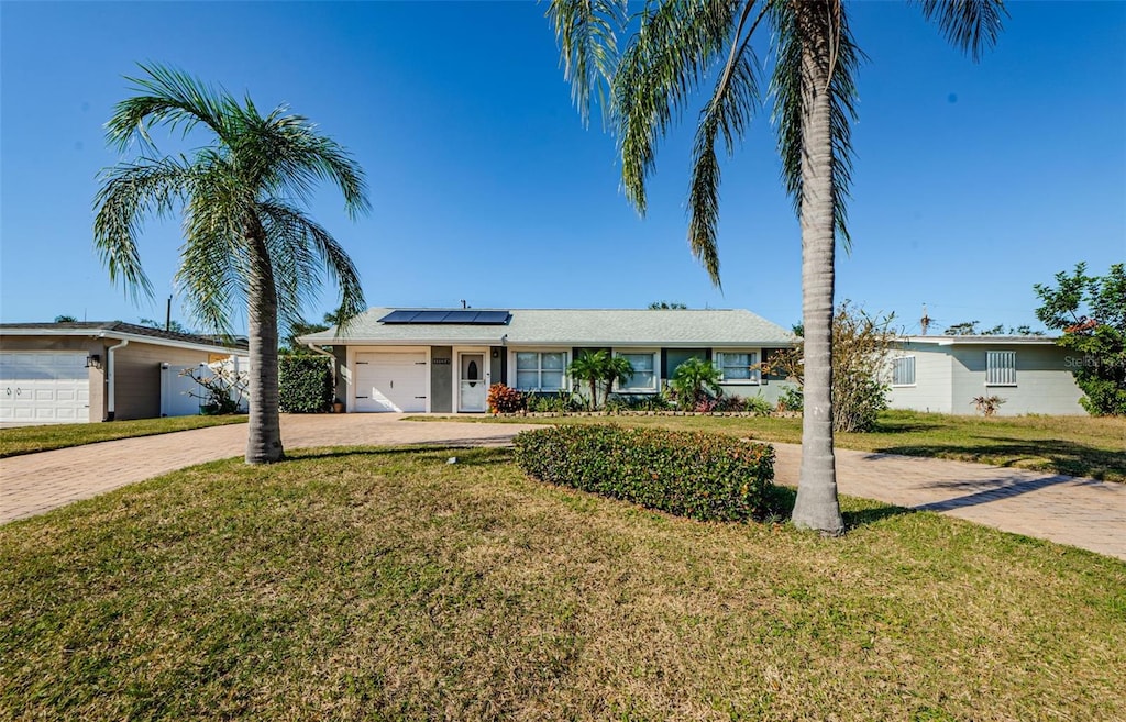 ranch-style home featuring a front yard, solar panels, and a garage