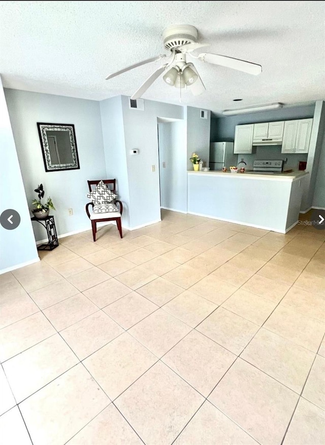 kitchen with light tile patterned floors, freestanding refrigerator, white cabinets, a textured ceiling, and a ceiling fan