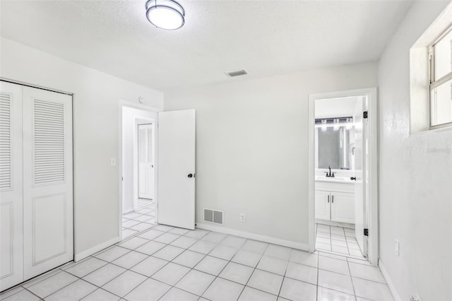 unfurnished bedroom featuring sink, ensuite bathroom, a textured ceiling, a closet, and light tile patterned flooring