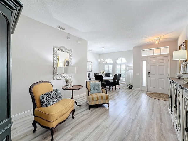 entrance foyer with a textured ceiling, light hardwood / wood-style floors, and an inviting chandelier