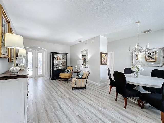 dining space featuring french doors, a chandelier, a textured ceiling, and light wood-type flooring