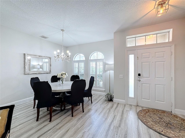 dining area with light wood-type flooring, a textured ceiling, and a chandelier