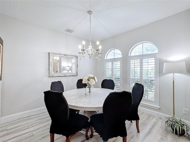 dining space with an inviting chandelier, a textured ceiling, and light hardwood / wood-style flooring