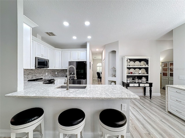 kitchen with a breakfast bar, white cabinets, black range oven, sink, and kitchen peninsula