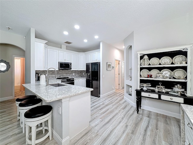 kitchen with white cabinets, sink, a textured ceiling, a kitchen bar, and stainless steel appliances