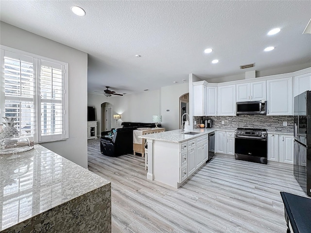 kitchen with sink, kitchen peninsula, white cabinets, black appliances, and light wood-type flooring