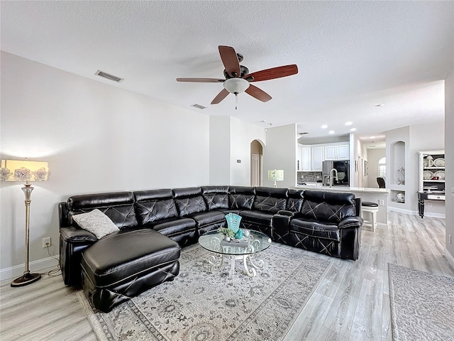 living room featuring ceiling fan, light hardwood / wood-style floors, and a textured ceiling