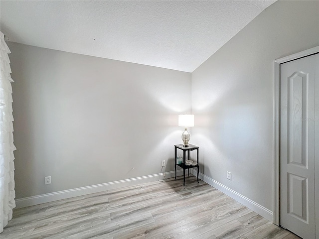 unfurnished room with a textured ceiling, light hardwood / wood-style flooring, and lofted ceiling